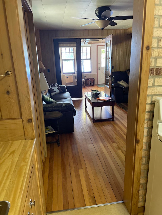 living room with washer / dryer, ceiling fan, hardwood / wood-style floors, and wooden walls