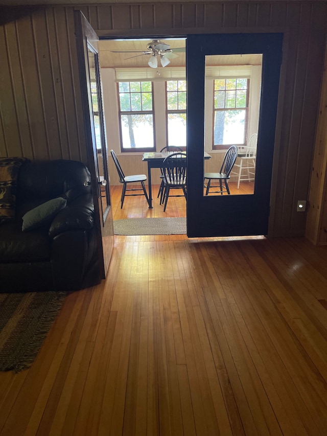 dining room with hardwood / wood-style floors, ceiling fan, a healthy amount of sunlight, and wood walls