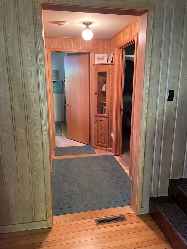 hallway with light hardwood / wood-style flooring and wooden walls