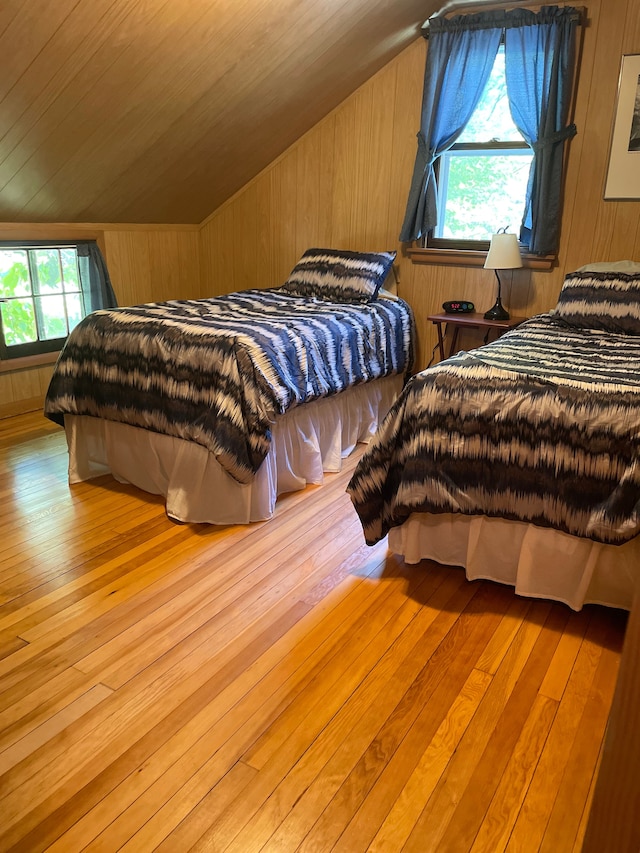 bedroom featuring multiple windows, wooden walls, light hardwood / wood-style floors, and vaulted ceiling