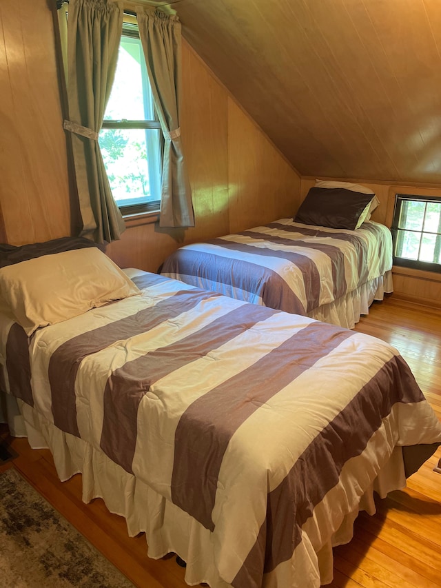 bedroom with light wood-type flooring, wooden walls, and lofted ceiling