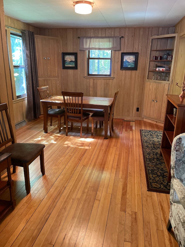 dining area with built in shelves, light wood-type flooring, a wealth of natural light, and wood walls