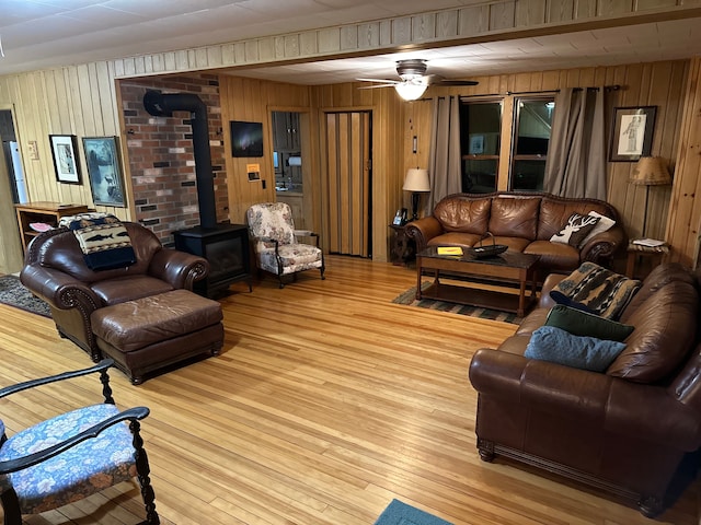 living room with ceiling fan, a wood stove, wooden walls, and light hardwood / wood-style flooring