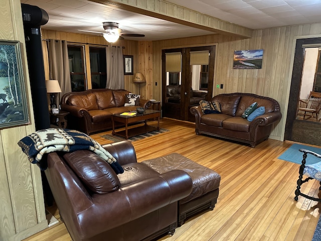 living room featuring light wood-type flooring, ceiling fan, and wood walls