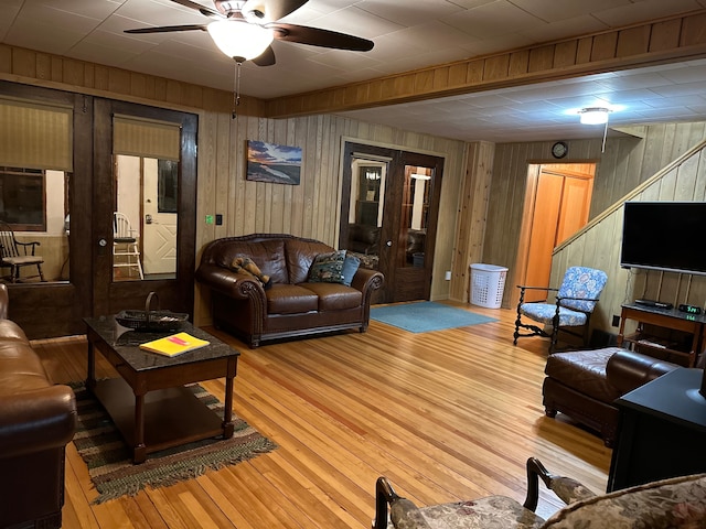 living room featuring light wood-type flooring, ceiling fan, and wood walls