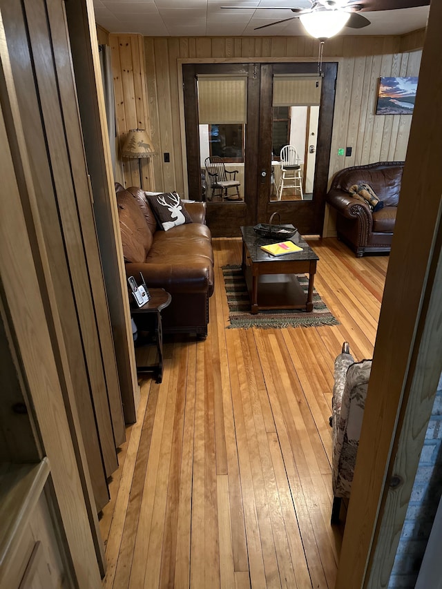 living room featuring ceiling fan, wooden walls, and light hardwood / wood-style flooring