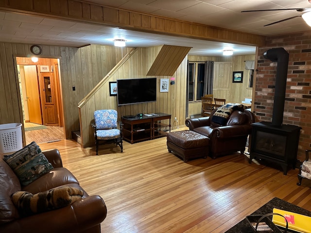 living room with ceiling fan, wood walls, a wood stove, and light hardwood / wood-style flooring