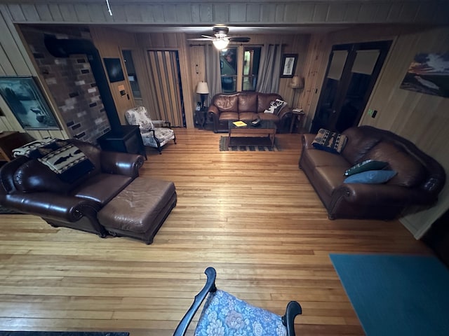 living room featuring hardwood / wood-style flooring, ceiling fan, a wood stove, and wooden walls