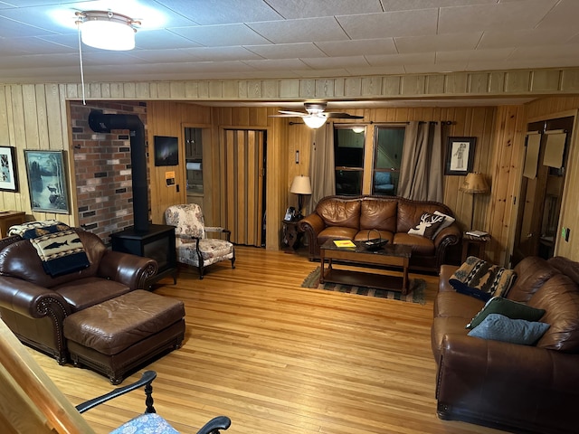 living room with hardwood / wood-style floors, a wood stove, ceiling fan, and wooden walls