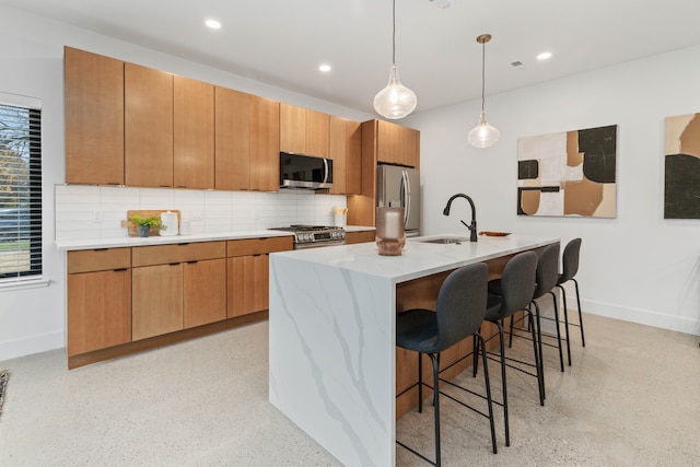 kitchen featuring sink, stainless steel appliances, an island with sink, decorative light fixtures, and decorative backsplash