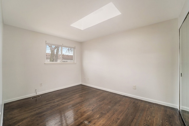 empty room with a skylight and dark hardwood / wood-style floors