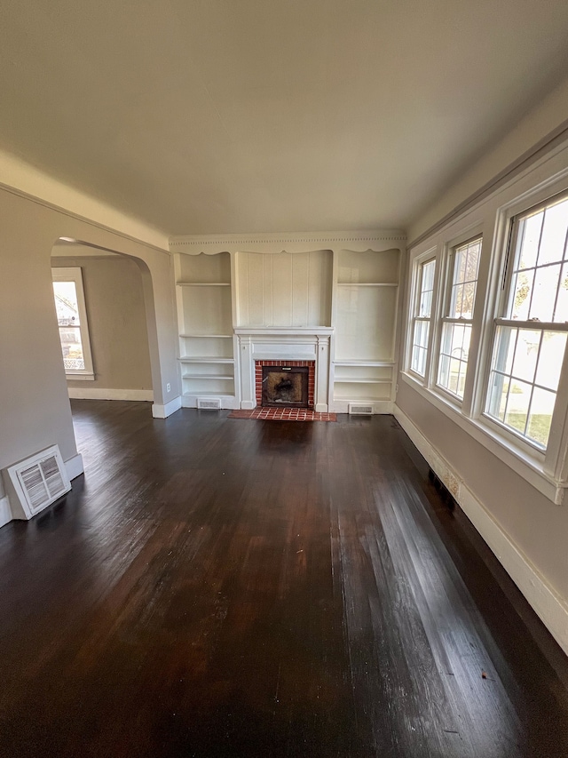 unfurnished living room featuring dark hardwood / wood-style flooring, built in features, and a brick fireplace