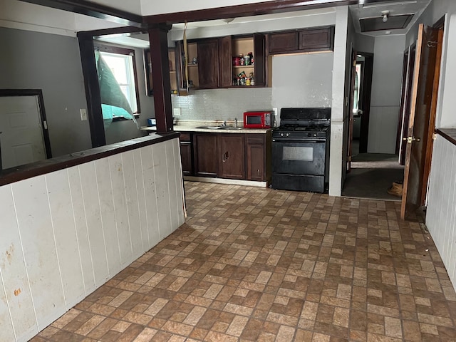 kitchen featuring tasteful backsplash, dark brown cabinets, wooden walls, sink, and black appliances