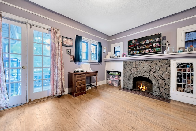 living room with a stone fireplace, wood-type flooring, and a textured ceiling