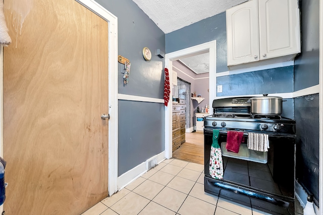 kitchen with black gas range, a textured ceiling, white cabinetry, and light tile patterned flooring