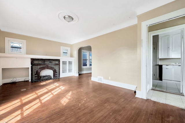 unfurnished living room featuring wood-type flooring and a brick fireplace