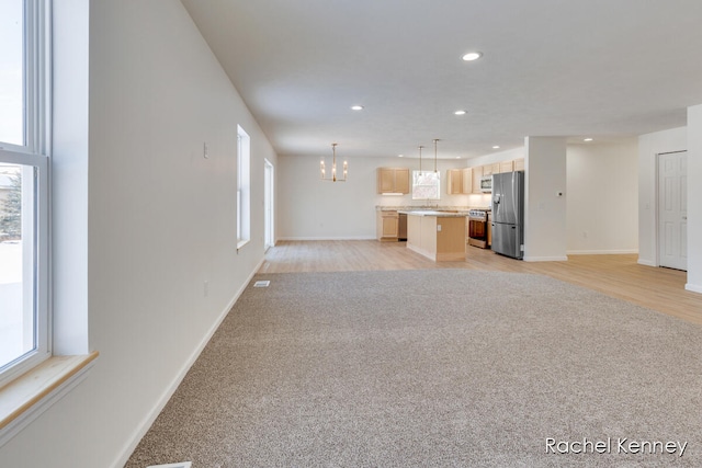 unfurnished living room with a notable chandelier, a healthy amount of sunlight, sink, and light hardwood / wood-style flooring