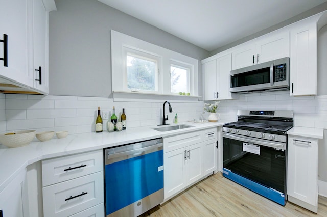 kitchen with sink, stainless steel appliances, light hardwood / wood-style flooring, decorative backsplash, and white cabinets