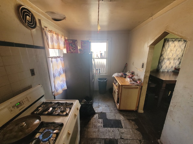 kitchen featuring white range with gas stovetop, stainless steel fridge, and tile walls