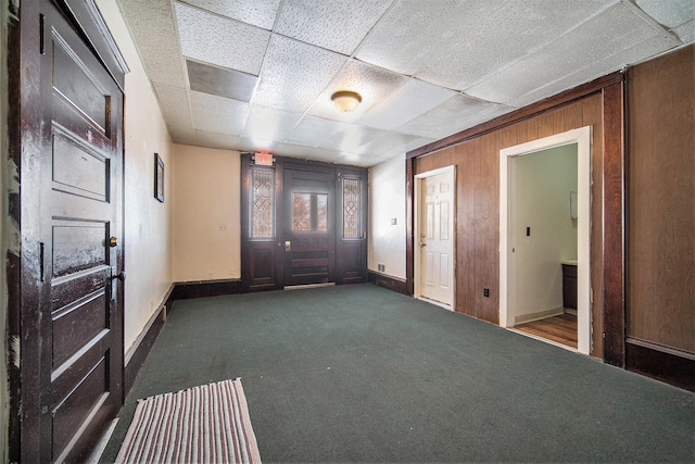 interior space featuring wood walls, a drop ceiling, and dark carpet