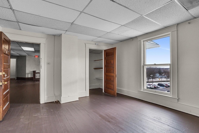 unfurnished bedroom with a paneled ceiling, a closet, and dark wood-type flooring