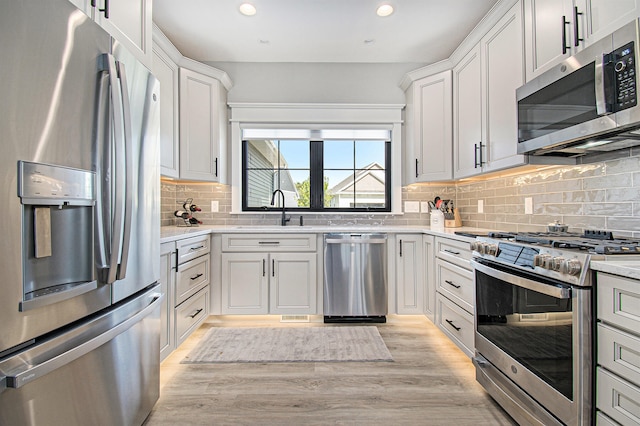 kitchen with appliances with stainless steel finishes, light hardwood / wood-style flooring, white cabinetry, and sink