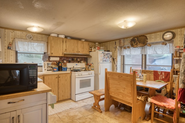 kitchen with tasteful backsplash, a textured ceiling, white appliances, light tile patterned floors, and wood walls