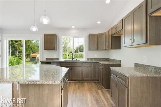 kitchen with a kitchen island, light stone countertops, sink, and light hardwood / wood-style flooring