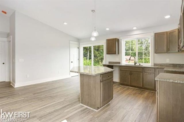 kitchen with pendant lighting, sink, vaulted ceiling, light hardwood / wood-style flooring, and a kitchen island