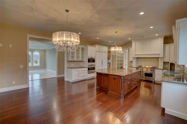 kitchen with appliances with stainless steel finishes, an island with sink, sink, white cabinets, and hanging light fixtures