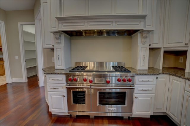 kitchen with custom exhaust hood, dark stone counters, white cabinets, and range with two ovens