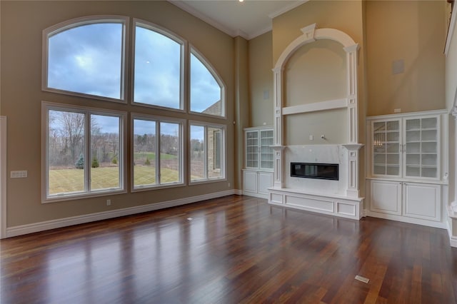 unfurnished living room featuring crown molding, dark hardwood / wood-style floors, a premium fireplace, and a high ceiling