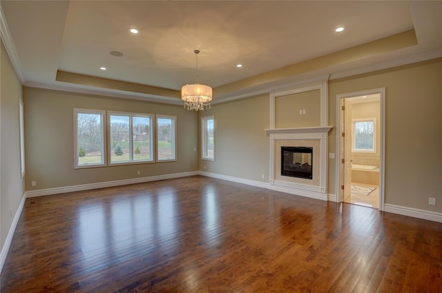 unfurnished living room featuring dark hardwood / wood-style flooring, a healthy amount of sunlight, a tray ceiling, and a chandelier