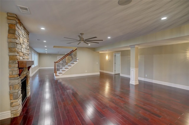 unfurnished living room featuring ornate columns, ceiling fan, a fireplace, and dark hardwood / wood-style flooring