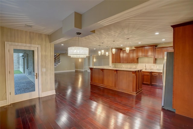 kitchen featuring a kitchen island, a breakfast bar, pendant lighting, stainless steel refrigerator, and dark wood-type flooring