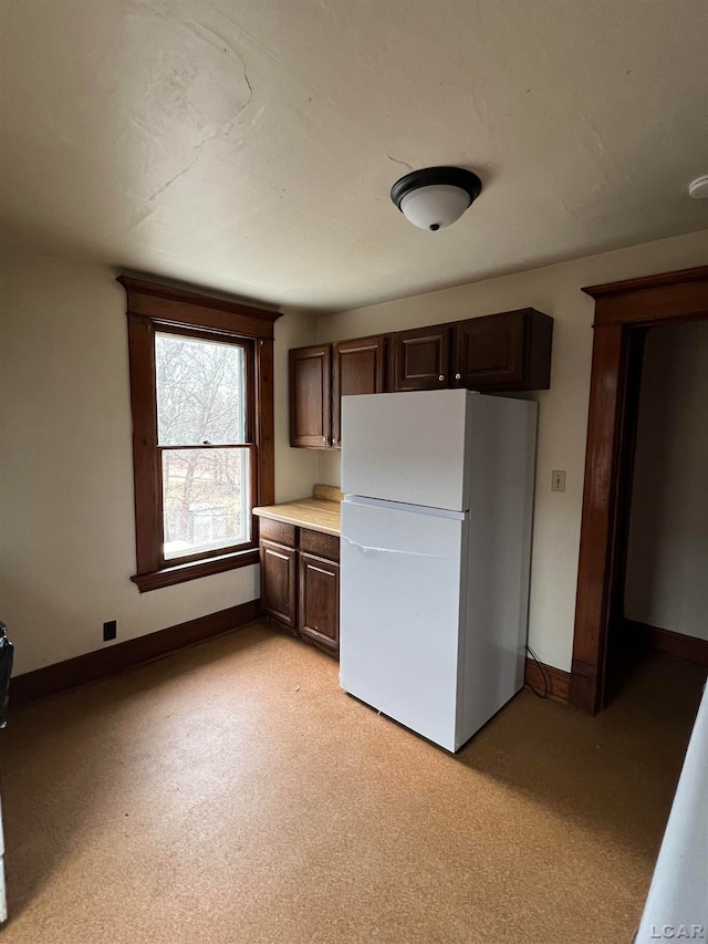 kitchen featuring white refrigerator, light colored carpet, and dark brown cabinetry