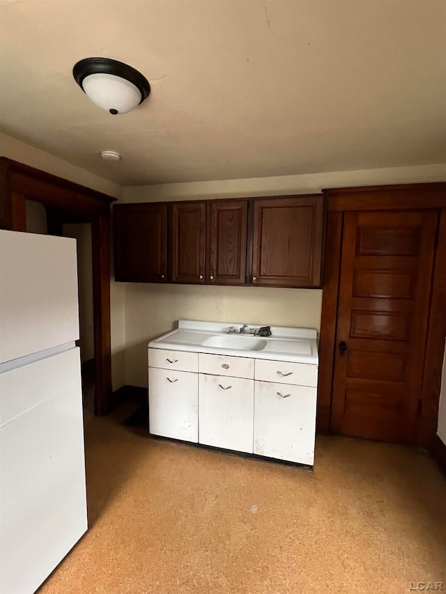 kitchen featuring white refrigerator, dark brown cabinetry, and sink