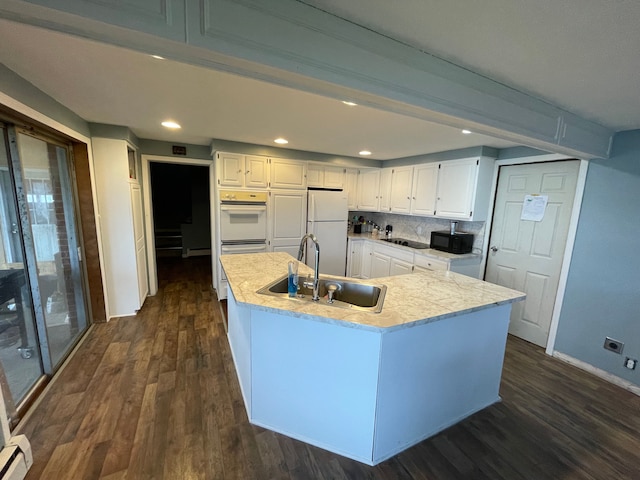 kitchen featuring white appliances, dark wood-type flooring, sink, a center island with sink, and white cabinetry