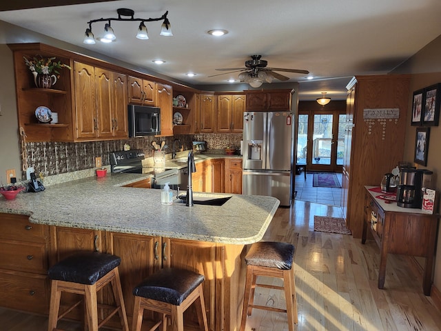 kitchen featuring kitchen peninsula, stainless steel refrigerator with ice dispenser, hardwood / wood-style flooring, black electric range, and a breakfast bar area