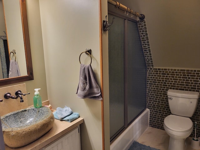 full bathroom featuring bath / shower combo with glass door, vanity, tile walls, tile patterned flooring, and toilet