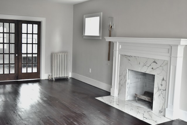 unfurnished living room featuring french doors, dark hardwood / wood-style flooring, radiator, and a premium fireplace