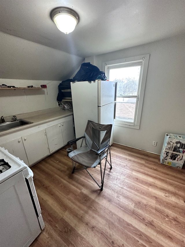 interior space with stove, white cabinets, sink, vaulted ceiling, and light hardwood / wood-style floors