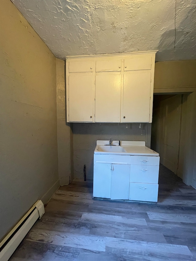 kitchen featuring sink, white cabinets, a baseboard radiator, and hardwood / wood-style flooring