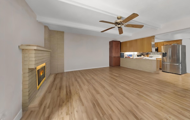 unfurnished living room featuring beamed ceiling, ceiling fan, a brick fireplace, and light hardwood / wood-style floors