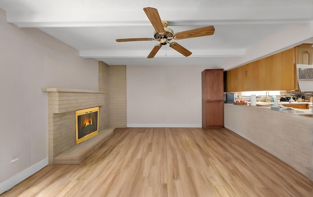 unfurnished living room featuring beam ceiling, a brick fireplace, and light hardwood / wood-style flooring