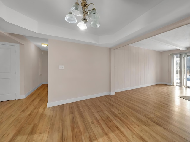 empty room featuring an inviting chandelier, a raised ceiling, light wood-type flooring, and beam ceiling