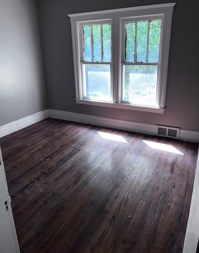 empty room featuring dark wood-type flooring and a healthy amount of sunlight