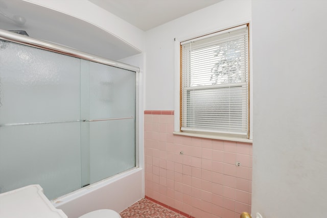 bathroom featuring toilet, tile walls, and bath / shower combo with glass door