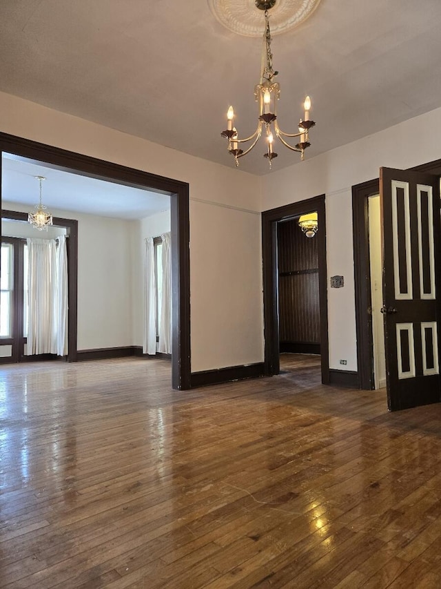 unfurnished dining area with wood-type flooring, a notable chandelier, and baseboards