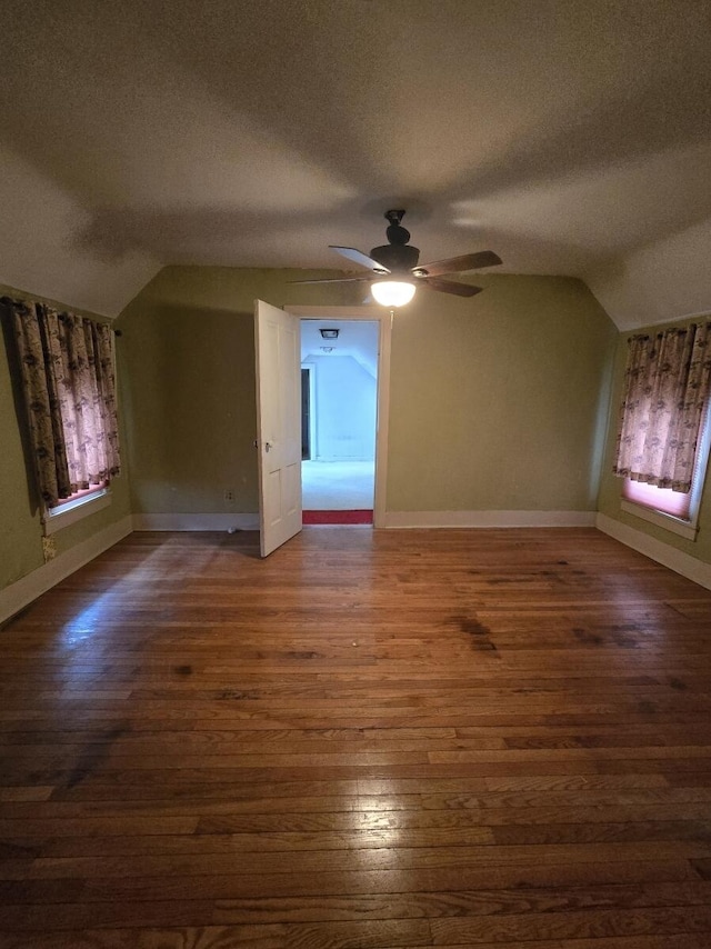 additional living space featuring dark wood-style flooring, baseboards, vaulted ceiling, a textured ceiling, and ceiling fan